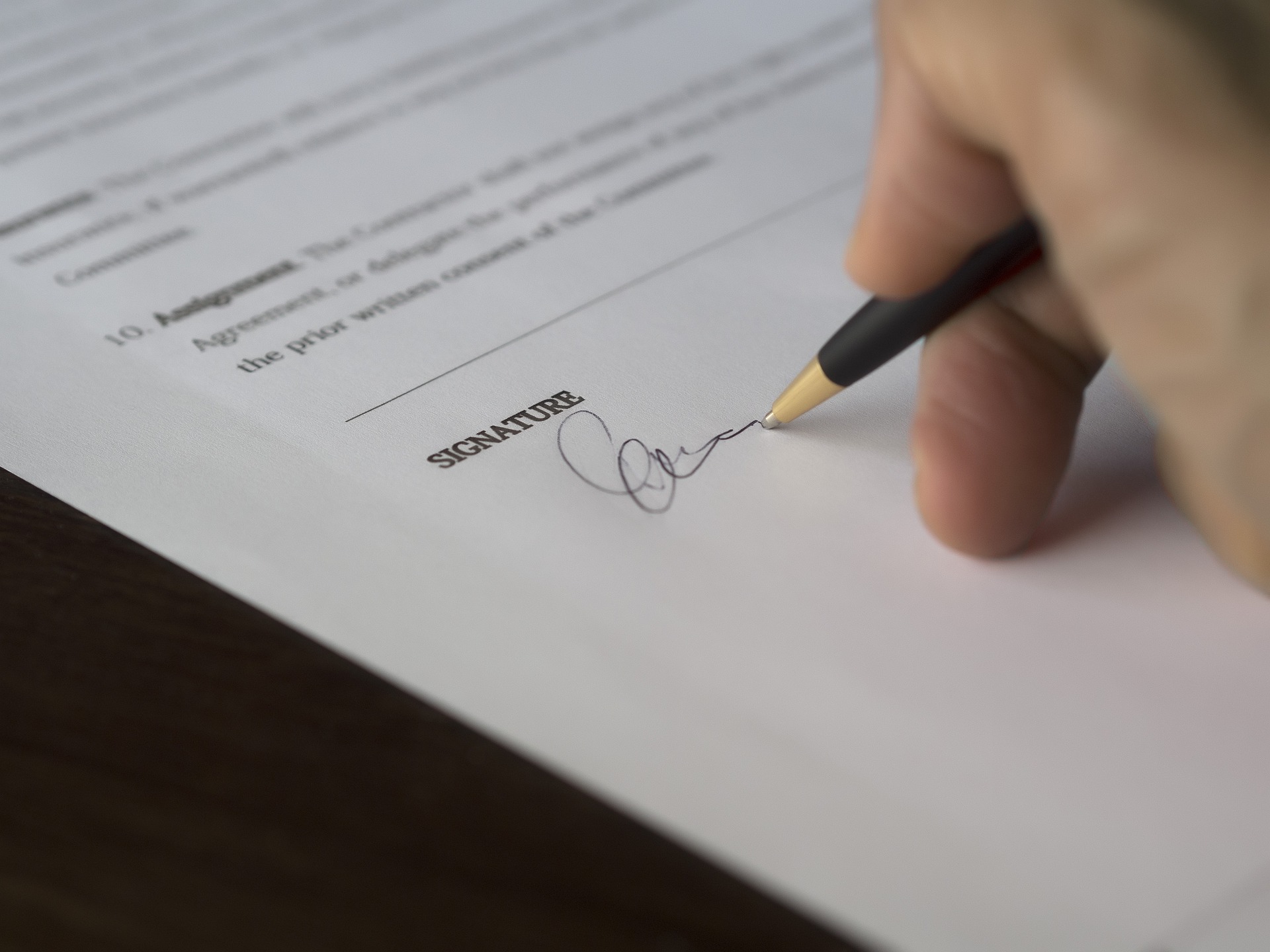 fragment dłoni i dokumentu - umowy, osoba trzyma w dłoni długopis i podisuje umowę 